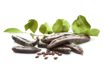 Carob, white background. Organic carob pods with seeds and green leaves. Healthy eating, food background.
