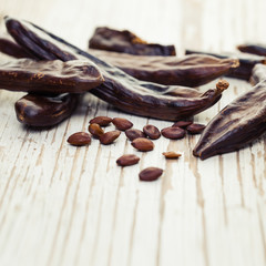 Carob. Healthy organic sweet carob pods and seeds on white wooden background closeup.