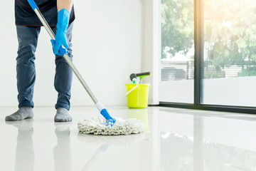 Young housekeeper cleaning floor mobbing holding mop and plastic bucket with brushes, gloves and...