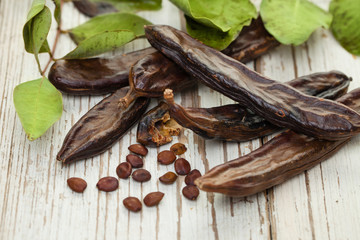 Carob pods. Healthy organic sweet carob pods with seeds and green leaves on a wooden table. Healthy eating, food background.