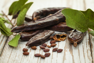 Carob beans. Healthy organic sweet carob pods with seeds and leaves on a wooden board. Healthy eating, food background.