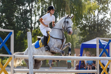Equestrian sport. Young girl jumping over obstacle