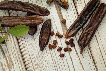 Organic carob pods with seeds and leaves on white wooden background, top view with copy space
