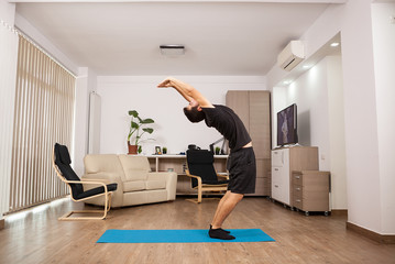 Attractive man with beard doing back stretch standing up. Adult working out.