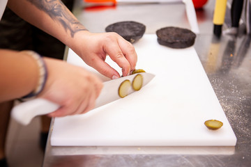 Obraz na płótnie Canvas Chef slices pickles for delicious burger in restaurant. Food preparation