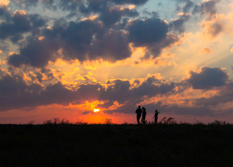Obraz na płótnie Canvas sunset dawn sun rays over field sky field family walking near the sun on the horizon silhouette