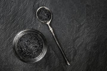 An overhead photo of black caviar in a jar and in a spoon, shot from above on a black background...