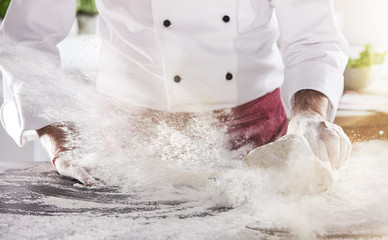Flour spraying into air as chef rolls dough ball