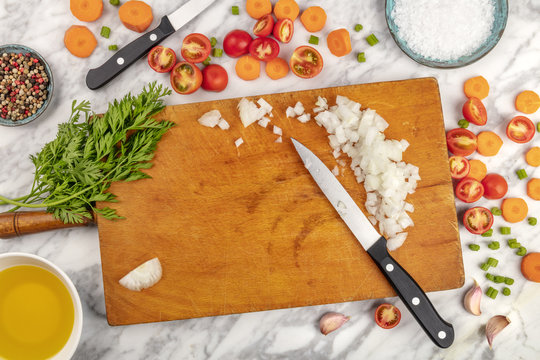 Prep time, or mise en place. An overhead photo of professional chef's knives, shot from above on a cutting board, with chopped vegetables and spices, on a marble cooking surface with copy space