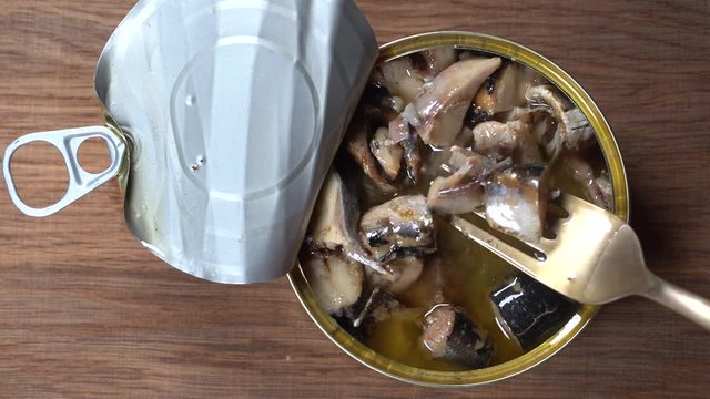 Using fork takes a sardines fish, sardines in oil sauce from a tin can. Top view, close up, macro
