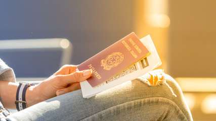 Italian passport and boarding pass in the hands of woman awaiting departure flight in waiting hall - concept of independence and easy traveling in Europe - obrazy, fototapety, plakaty