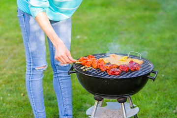 Young woman is making meat barbecue in the garden on the green grass - cooking healthy organic and...