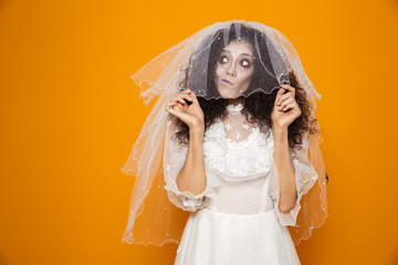 Thoughtful zombie bride looking up and holding veil isolated