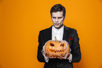 Displeased zombie man holding pumpkin and looking aside