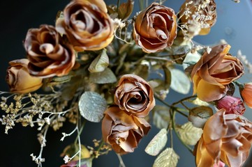 A top view close up of autumn brown colored artificial roses on black background. Intentional underexposed.