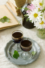 Obraz na płótnie Canvas Cream de Cassis homemade blackcurrant liqueur in small glasses, books and flowers. Rustic style.