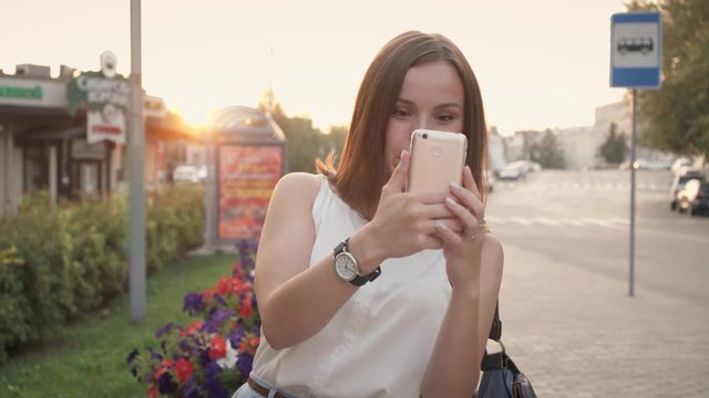 The girl is taking pictures on the street using a smartphone.
