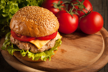 Home made hamburger with beef, onion, tomato, lettuce and cheese. Fresh burger close up on wooden rustic table with potato fries, beer and chips. Cheeseburger.