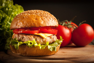 Home made hamburger with beef, onion, tomato, lettuce and cheese. Fresh burger close up on wooden rustic table with potato fries, beer and chips. Cheeseburger.