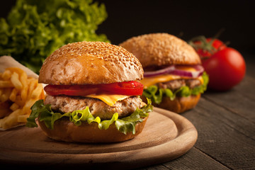 Home made hamburger with beef, onion, tomato, lettuce and cheese. Fresh burger close up on wooden rustic table with potato fries, beer and chips. Cheeseburger.