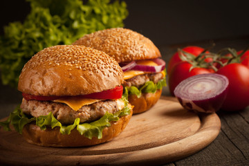 Home made hamburger with beef, onion, tomato, lettuce and cheese. Fresh burger close up on wooden rustic table with potato fries, beer and chips. Cheeseburger.