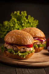 Home made hamburger with beef, onion, tomato, lettuce and cheese. Fresh burger close up on wooden rustic table with potato fries, beer and chips. Cheeseburger.