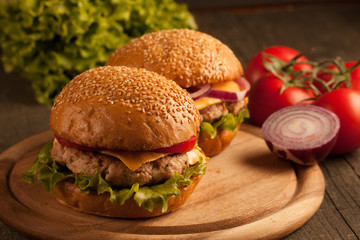 Home made hamburger with beef, onion, tomato, lettuce and cheese. Fresh burger close up on wooden rustic table with potato fries, beer and chips. Cheeseburger.