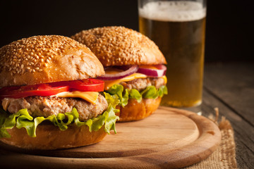 Home made hamburger with beef, onion, tomato, lettuce and cheese. Fresh burger close up on wooden rustic table with potato fries, beer and chips. Cheeseburger.