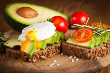 Avocado toast, cherry tomato and poached eggs on wooden background. Breakfast with vegetarian food, healthy diet concept.