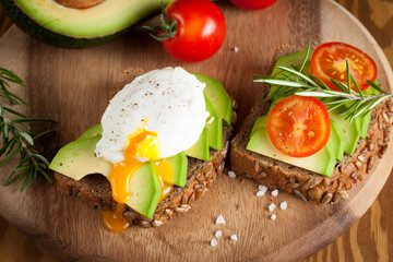 Avocado toast, cherry tomato and poached eggs on wooden background. Breakfast with vegetarian food, healthy diet concept.