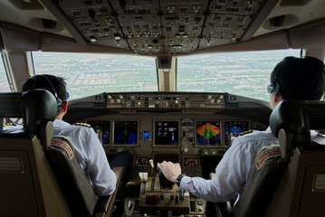 Two airliner pilots are controlling the airplane towards the runway. Seen from inside cockpit at observer seat behind pilots. Modern aviation concept. - obrazy, fototapety, plakaty