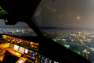 Inside cockpit of commercial airplane while flying over city in night time. Outside window can see...