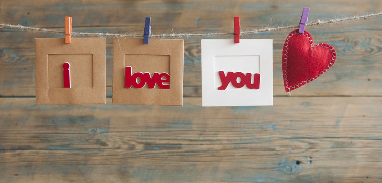 Paper photo frame with written message spelling I love you and red hearts hanging on rope