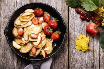 Cheese Buttermilk Pancakes or fritters with strawberry, sliced apples and coconut crunch on pan on vintage wooden table. Autumn breakfast