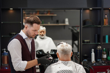 Hairdresser in black gloves trimming man's haircut.