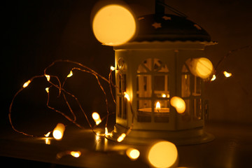 Glowing lantern in the shape of a house with Windows lit yellow. Festive interior decoration for the New year. Lights garlands and candles inside the lamp, glowing stars on the roof