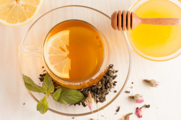 Closeup of cup of tea with tea leaves, mint on vintage wooden background. Black herbal tea with lemon, ginger and honey. hot winter drink