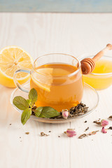 Closeup of cup of tea with tea leaves, mint on vintage wooden background. Black herbal tea with lemon, ginger and honey. hot winter drink
