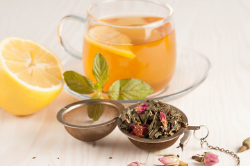 Closeup of cup of tea with tea leaves, mint on vintage wooden background. Black herbal tea with lemon, ginger and honey. hot winter drink