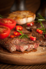grilled fillet steak with tomatoes and roast vegetables on an old wooden board, background.