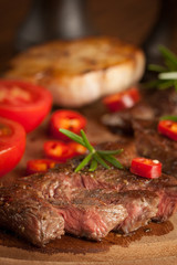 grilled fillet steak with tomatoes and roast vegetables on an old wooden board, background.