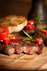 grilled fillet steak with tomatoes and roast vegetables on an old wooden board, background.