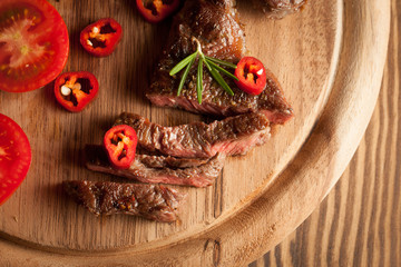 grilled fillet steak with tomatoes and roast vegetables on an old wooden board, background.