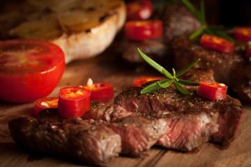 grilled fillet steak with tomatoes and roast vegetables on an old wooden board, background.