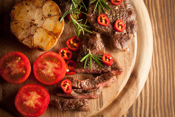 grilled fillet steak with tomatoes and roast vegetables on an old wooden board, background.