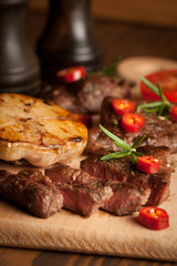 grilled fillet steak with tomatoes and roast vegetables on an old wooden board, background.