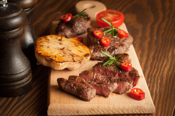 grilled fillet steak with tomatoes and roast vegetables on an old wooden board, background.