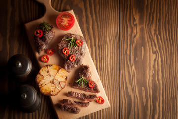 grilled fillet steak with tomatoes and roast vegetables on an old wooden board, background.