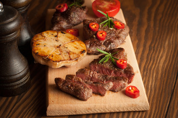 grilled fillet steak with tomatoes and roast vegetables on an old wooden board, background.