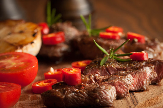 grilled fillet steak with tomatoes and roast vegetables on an old wooden board, background.